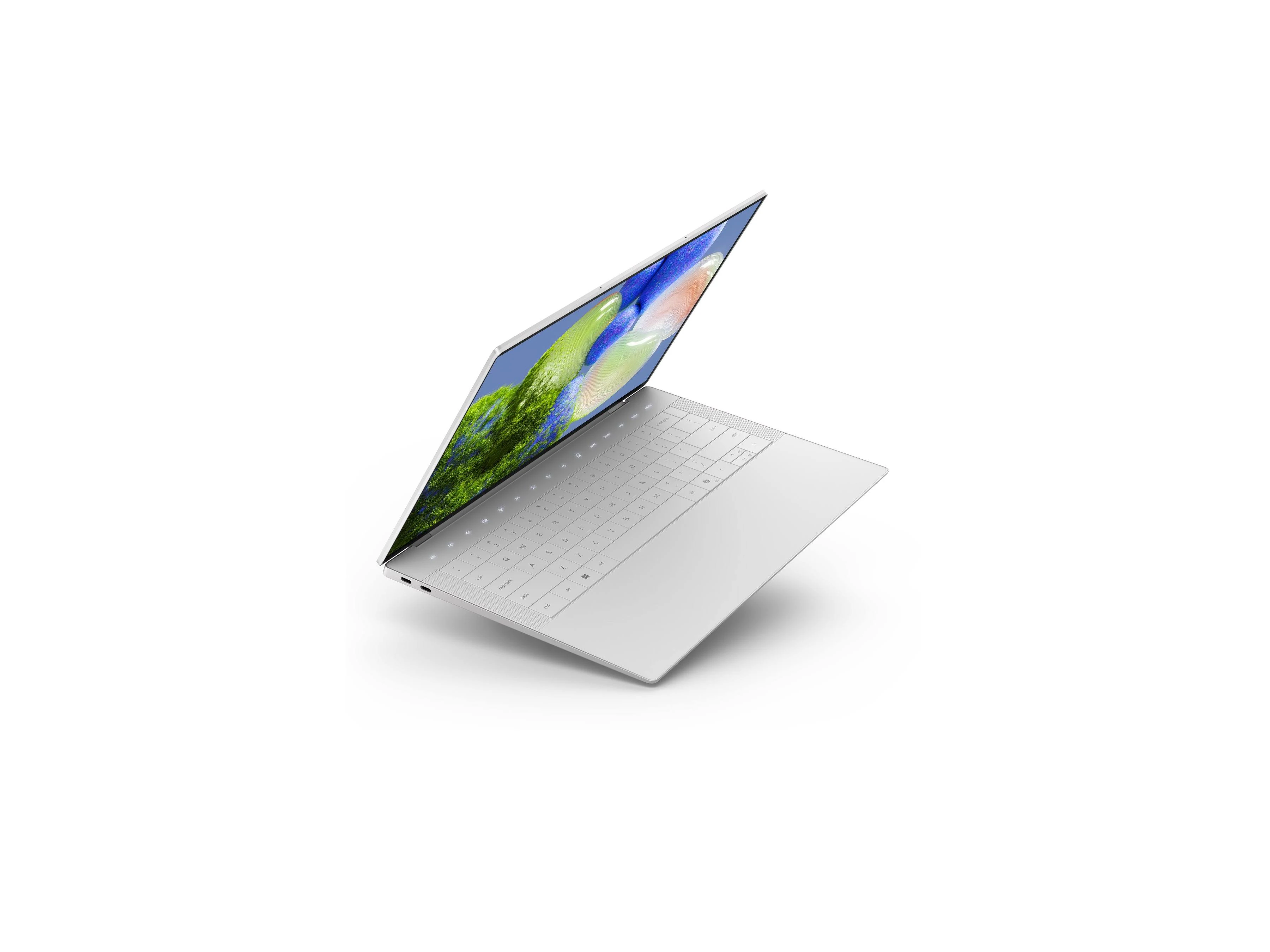 Seitenansicht aus der Vogelperspektive auf einen geöffneten Dell XPS Laptop in Silber. Gut sichtbar ist die flache Tastatur ohne physische Abgrenzung zwischen den Tasten und das nahtlose Glas-Touchpad. An der Seite befinden sich zwei USB-C-Anschlüsse.