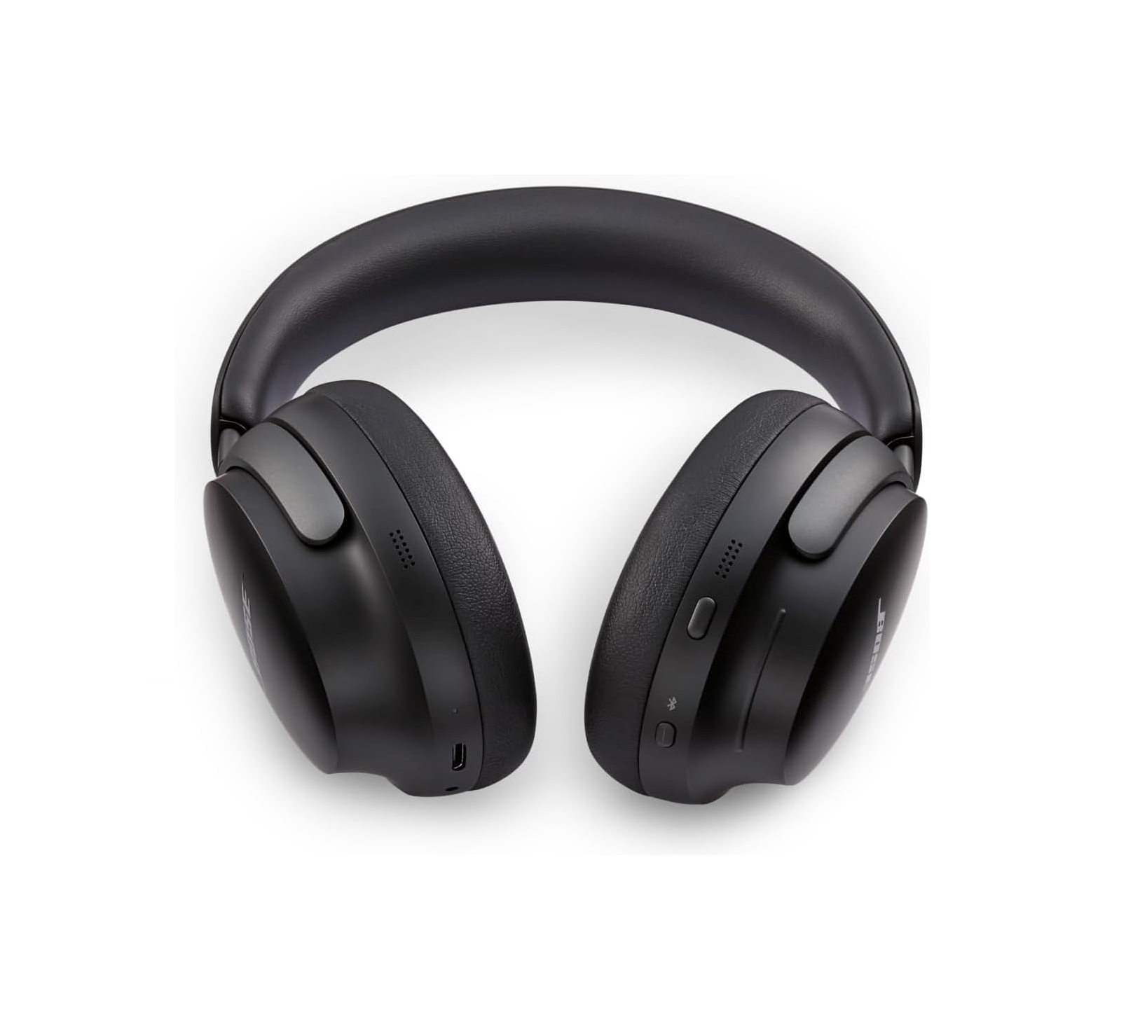 Eine Nahaufnahme von geschlossenen, mattschwarzen Bose QuietComfort Ultra Over-Ear-Kopfhörern mit gepolstertem Bügel, die auf weißem Hintergrund liegen. Die Außenseite der rechten Ohrmuschel zeigt sichtbare Steuerelemente.