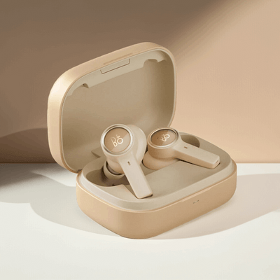 Bang & Olufsen BeoPlay EX True Wireless In-Ear-Kopfhörer in einer goldenen Farbvariante, platziert in ihrem geöffneten Ladeetui. Die Ohrhörer und das Etui haben ein monochromes, helles Finish mit einem leicht abgesetzten 'B&O'-Logo auf den Außenseiten.