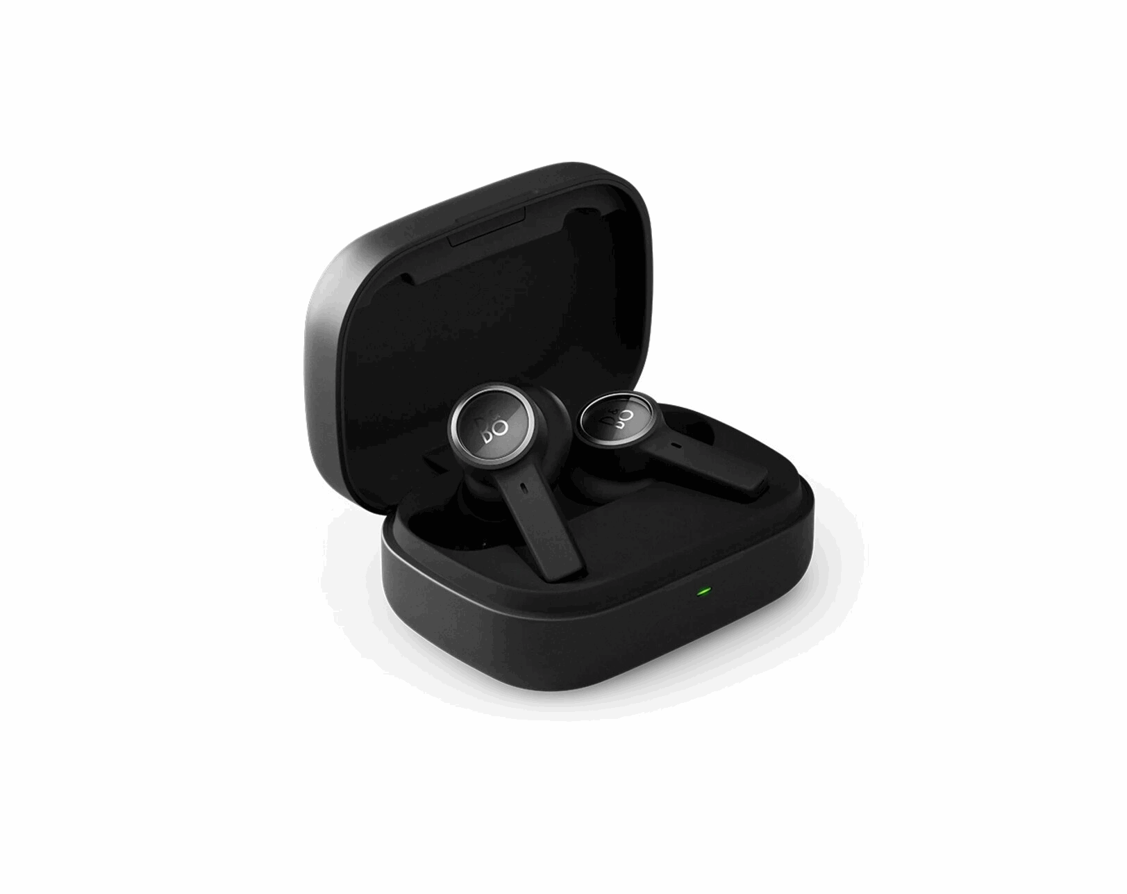 Nahaufnahme des geöffneten, mattschwarzen Ladeetuis der Bang & Olufsen BeoPlay EX Kopfhörer, platziert auf einer weißen Oberfläche. Die beiden anthrazitfarbenen Ohrhörer mit ihren silbernen 'B&O'-Logoplaketten liegen im Etui, das eine kleine grüne Ladeanzeige zeigt.